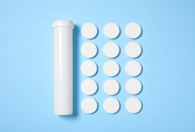 Container and pills on light blue background, flat lay