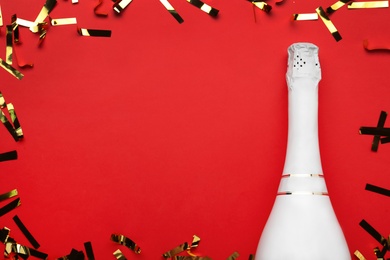 Photo of Flat lay composition with shiny confetti and bottle of champagne on red background, space for text