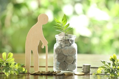 Photo of Pension savings. Figure of senior man, coins and green twigs on wooden table outdoors