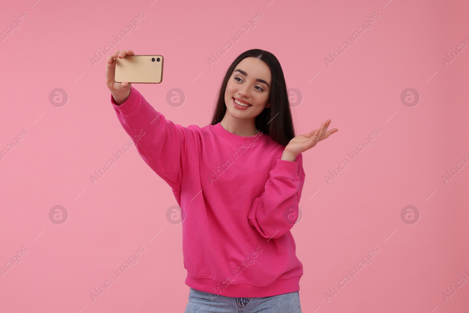 Photo of Smiling young woman taking selfie with smartphone on pink background