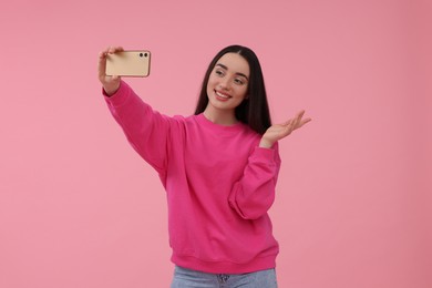 Photo of Smiling young woman taking selfie with smartphone on pink background