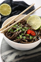 Photo of Tasty buckwheat noodles (soba) with sauce, onion in bowl and chopsticks on table