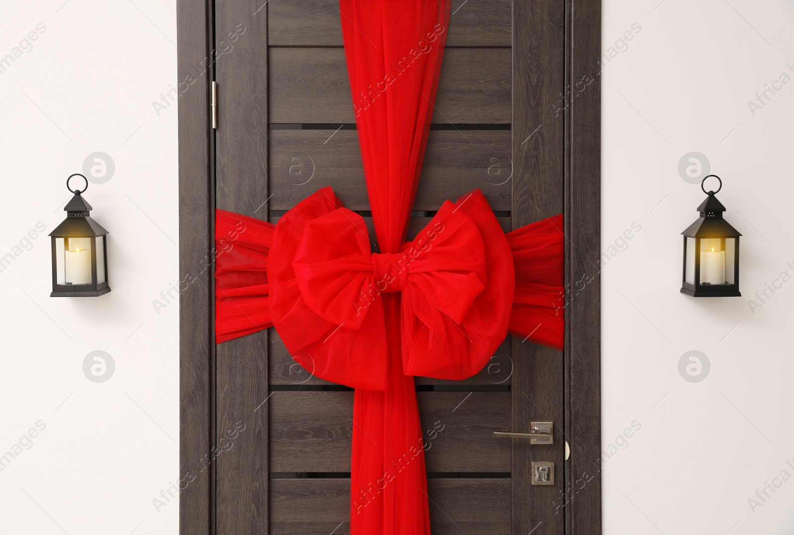 Photo of Wooden door with beautiful red bow and lanterns hanging on wall. Christmas decoration