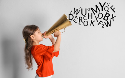 Image of Adorable little girl with vintage megaphone and letters on light background. Speech therapy concept