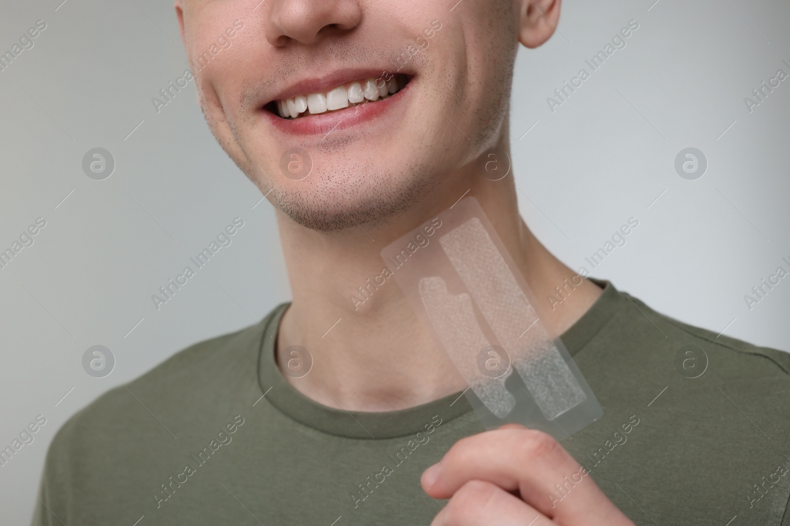 Photo of Young man with whitening strips on light grey background, closeup