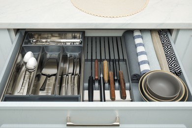 Photo of Open drawerkitchen cabinet with different utensils, dishware and towels