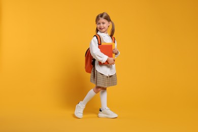 Photo of Happy schoolgirl with backpack and books on orange background