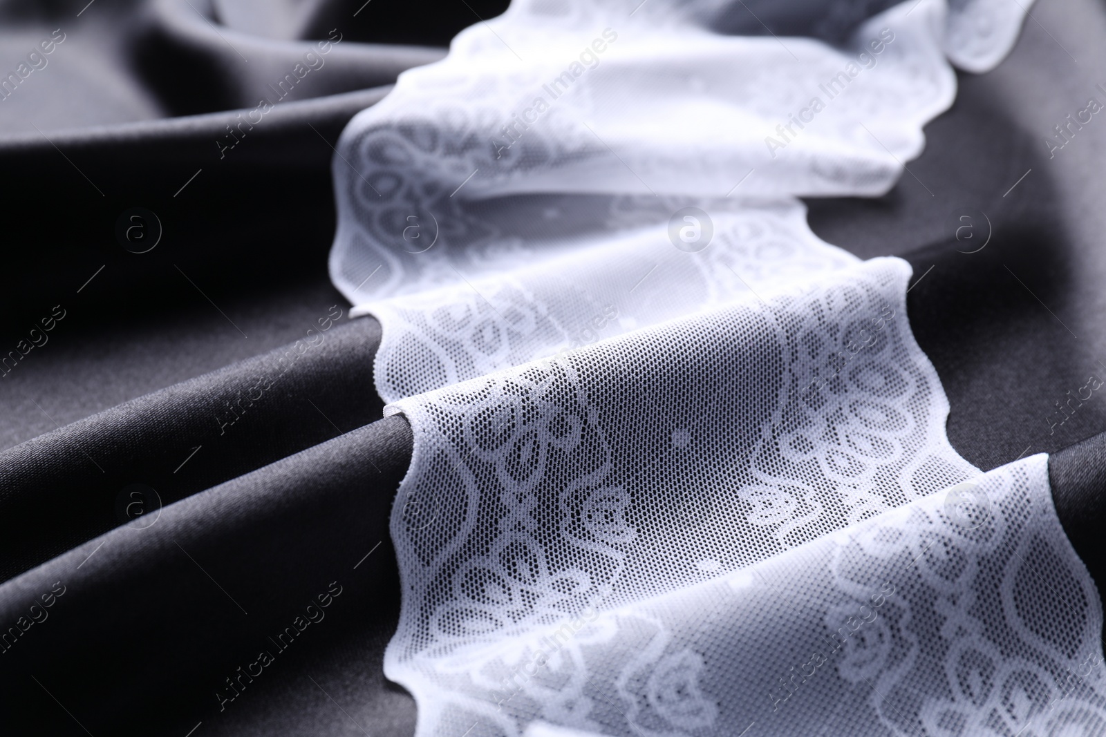 Photo of Beautiful white lace on black fabric, closeup