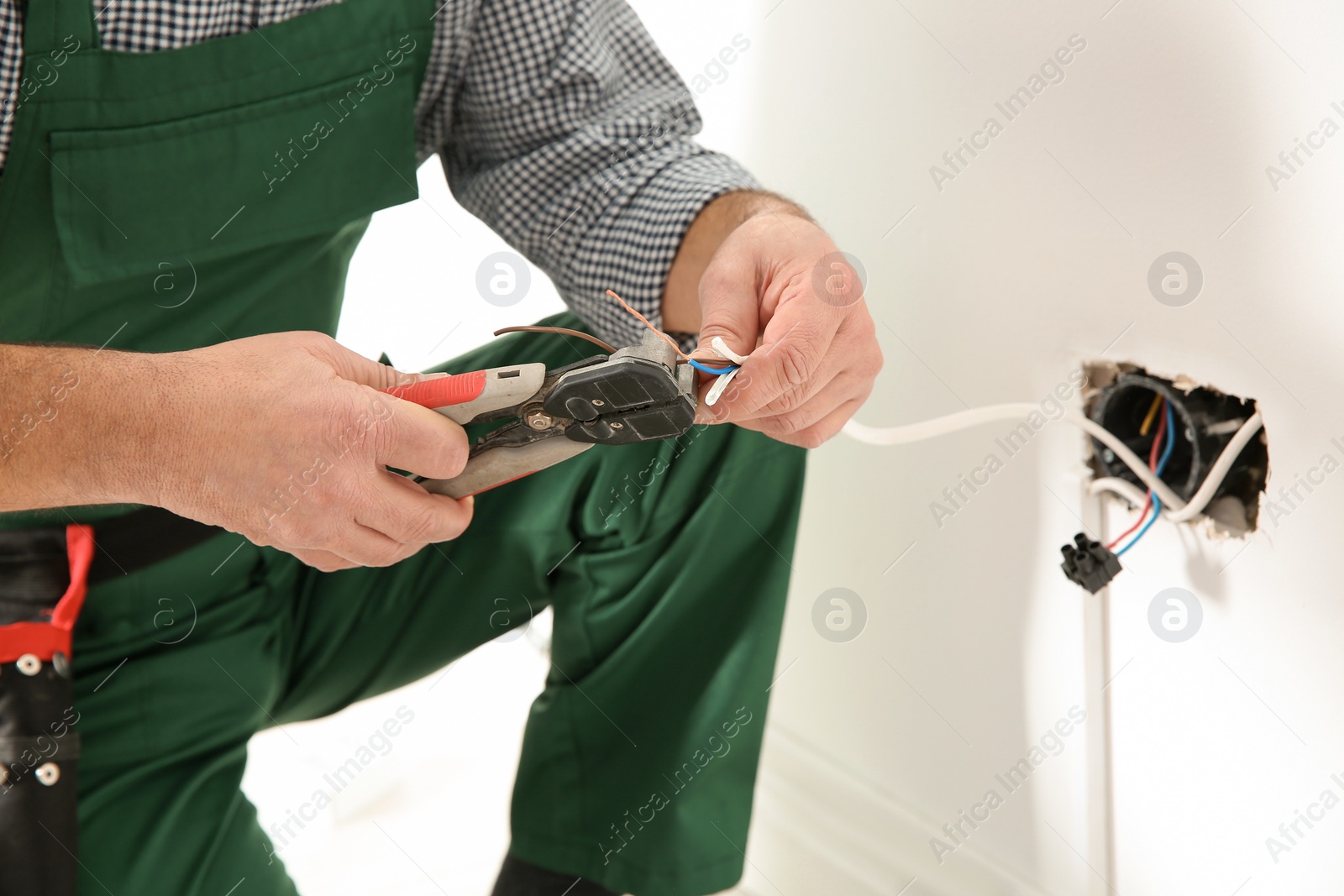 Photo of Professional electrician stripping wire ends indoors, closeup