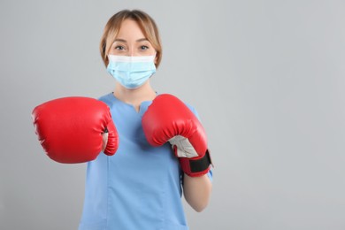 Photo of Doctor with protective mask and boxing gloves on light grey background, space for text. Strong immunity concept