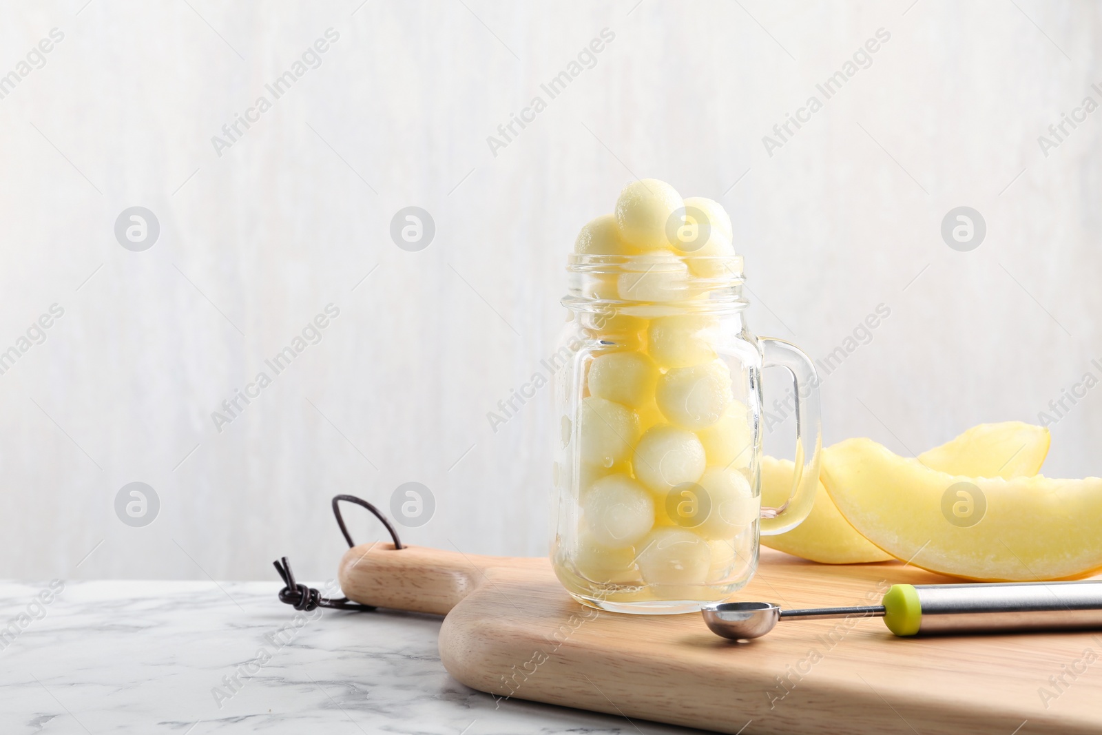 Photo of Mason jar with melon balls on white marble table. Space for text