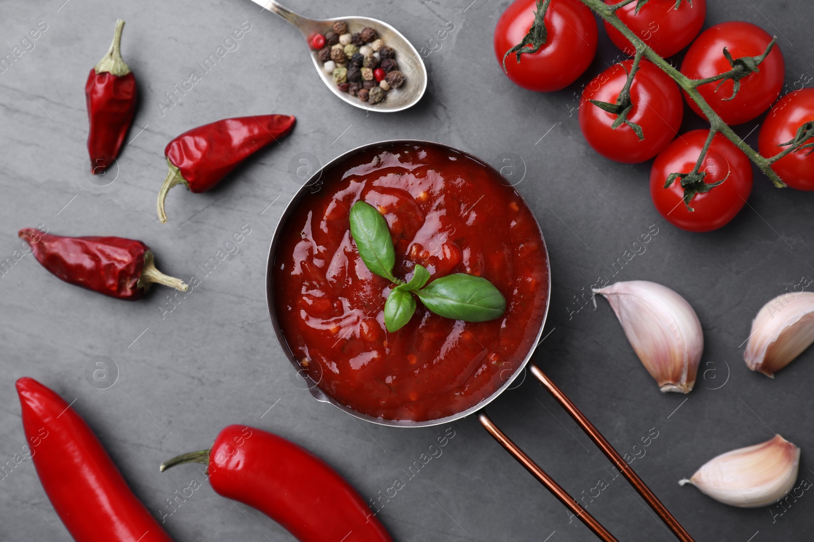 Photo of Flat lay composition with pan of chili sauce and ingredients on grey table
