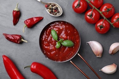 Flat lay composition with pan of chili sauce and ingredients on grey table