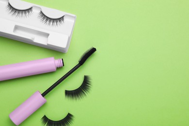 Photo of Flat lay composition with fake eyelashes and mascara brush on green background. Space for text