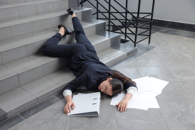 Photo of Unconscious woman with scattered folder and papers lying on floor after falling down stairs indoors