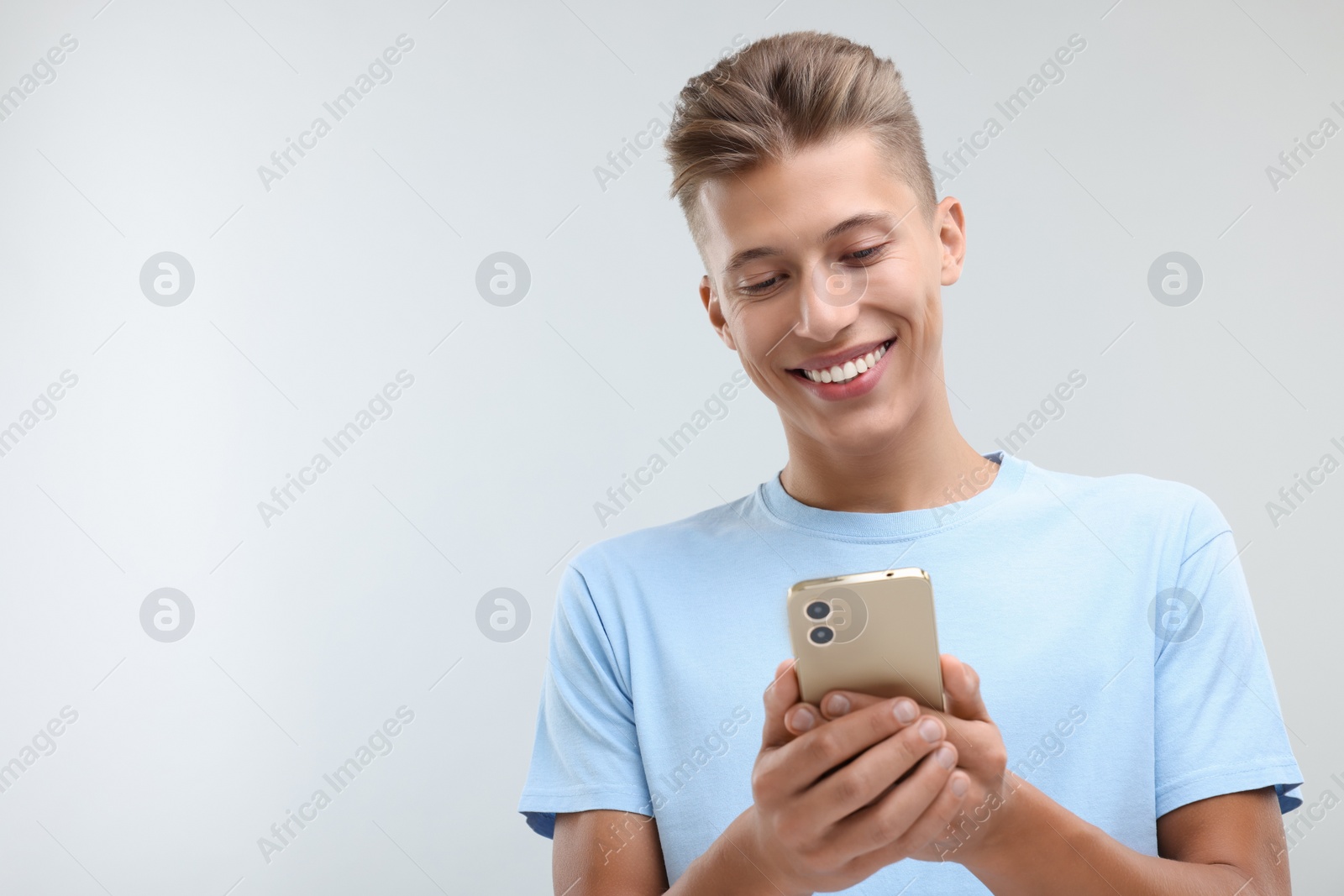Photo of Happy young man sending message via smartphone on light grey background. Space for text