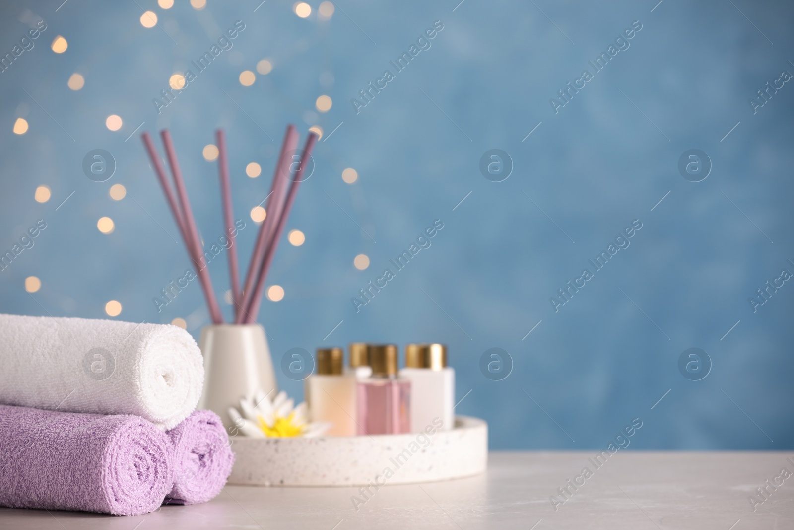 Photo of Stack of rolled towels and skin care products on light grey table. Space for text