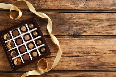 Different delicious chocolate candies in box and ribbon on wooden table, top view. Space for text