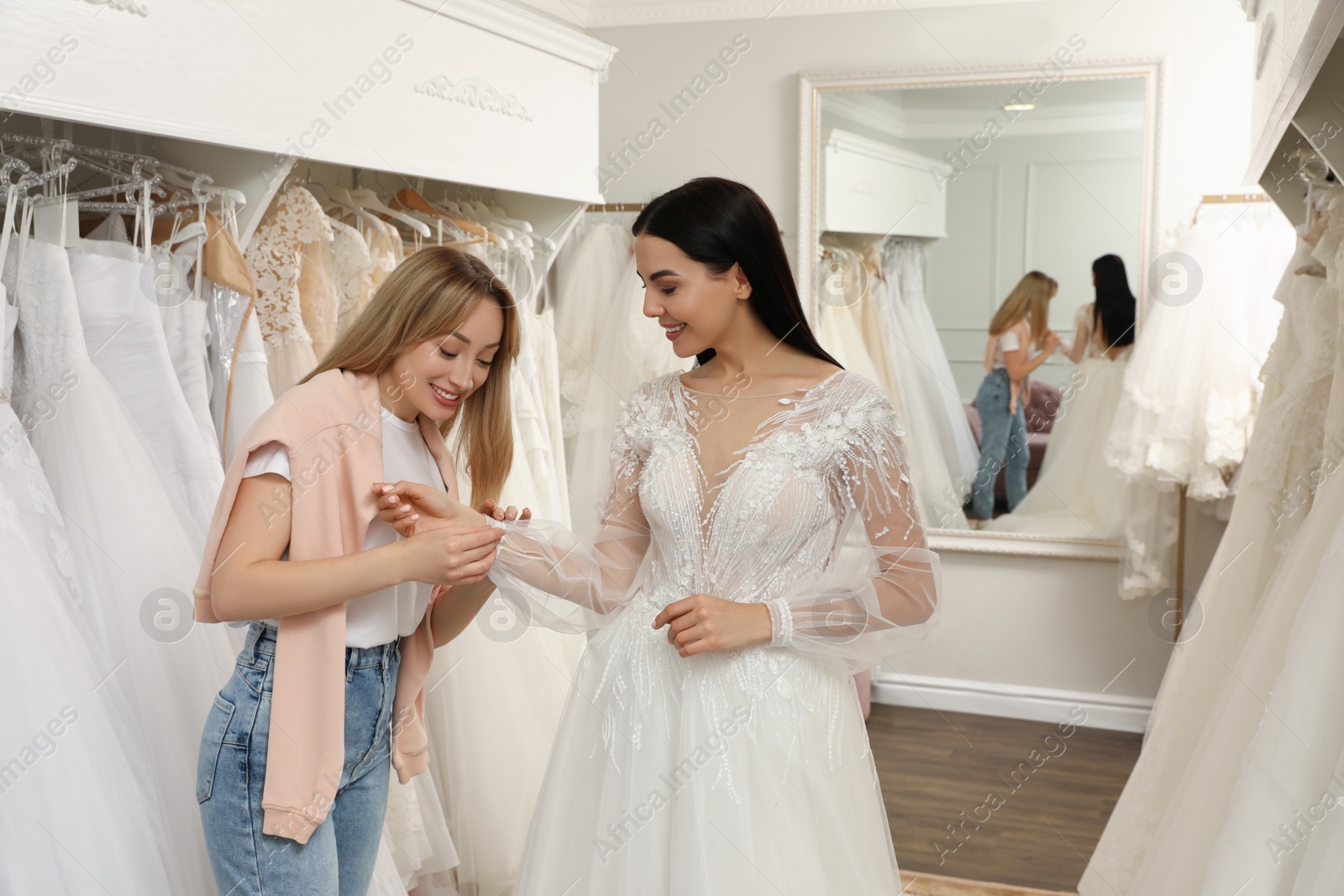 Photo of Woman helping bride wear wedding dress in boutique