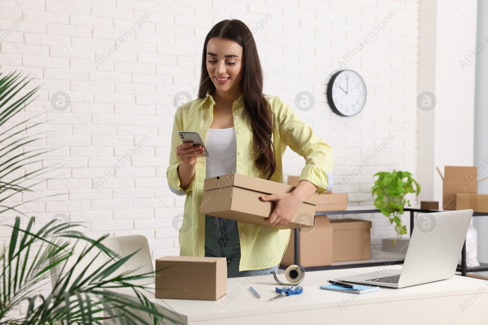 Photo of Seller with laptop and parcels using smartphone in office. Online store