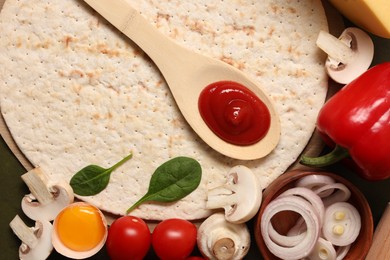 Photo of Pizza base, spoon with tomato sauce and products on dark table, flat lay