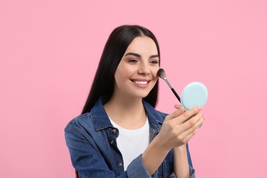 Photo of Beautiful woman with cosmetic pocket mirror applying makeup on pink background