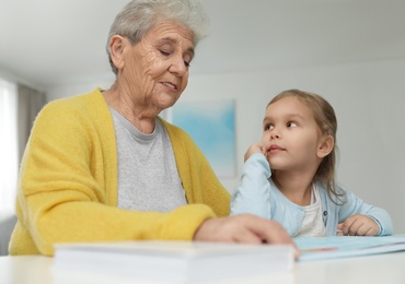 Photo of Cute girl and her grandmother reading book at home