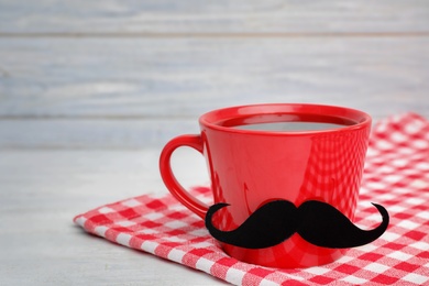 Red cup with paper moustache and space for text on wooden background. Father's day celebration