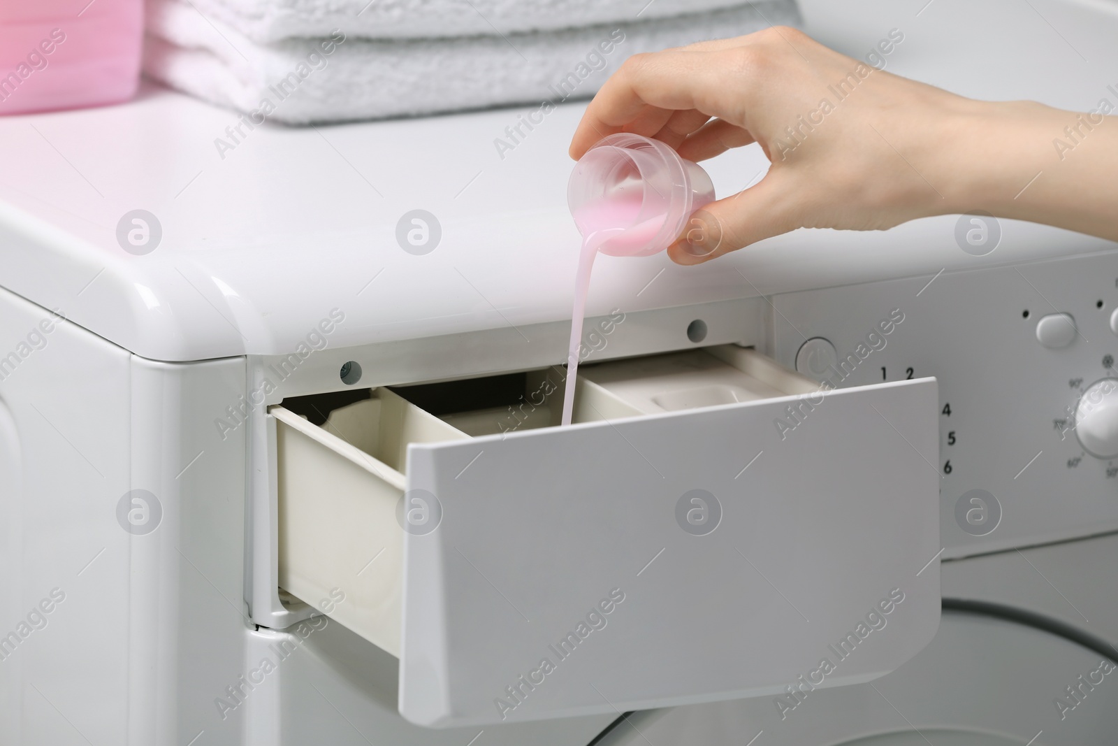 Woman pouring fabric softener from cap into washing machine, closeup Photo of Woman pouring fabric softener from cap into washing machine, closeup