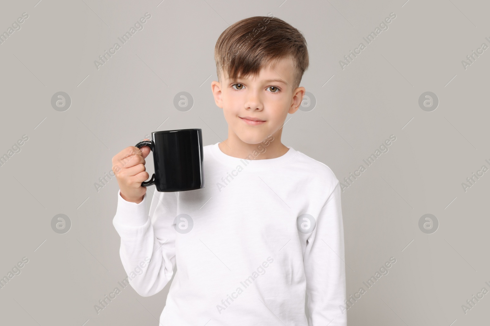 Photo of Cute boy with black ceramic mug on light grey background