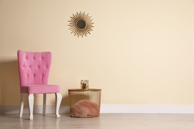 Stylish pink chair and table near beige wall in room. Space for text