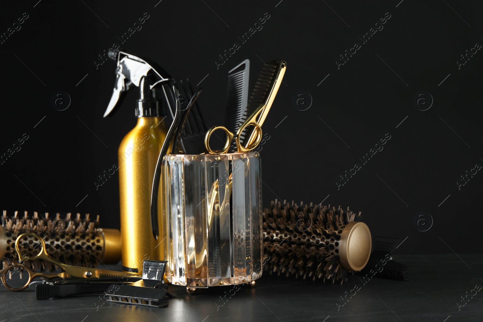 Photo of Different hairdresser tools on grey table against black background. Space for text