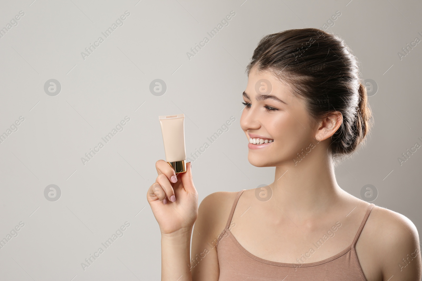 Photo of Beautiful girl with tube of foundation on light grey background