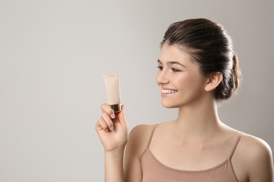 Beautiful girl with tube of foundation on light grey background