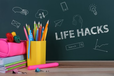 Words Life Hacks and drawings on green chalkboard near wooden table with stationery
