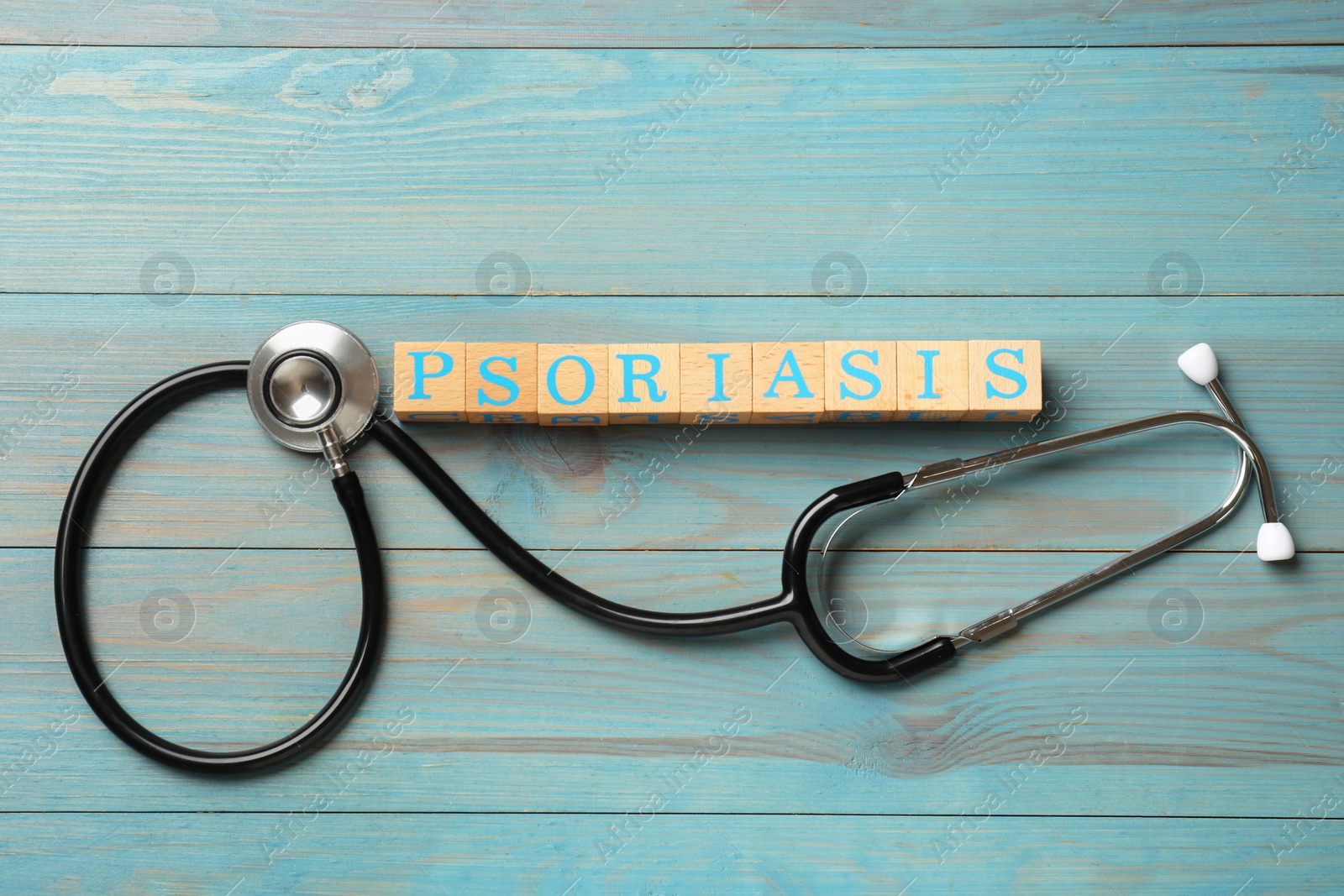 Photo of Word Psoriasis made of cubes with letters and stethoscope on light blue wooden table, flat lay