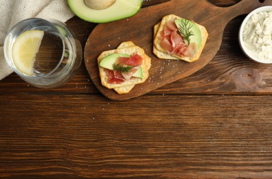 Photo of Delicious crackers with avocado, prosciutto and dill on wooden table, flat lay. Space for text