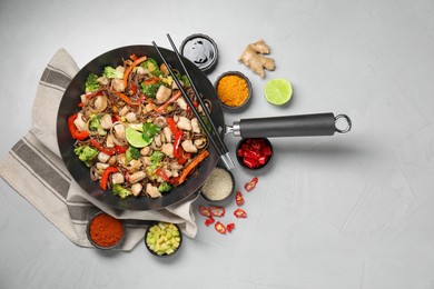 Stir-fry. Tasty noodles with meat in wok, chopsticks and ingredients on grey textured table, flat lay