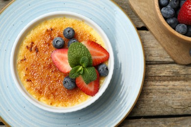 Delicious creme brulee with berries and mint in bowl on wooden table, top view