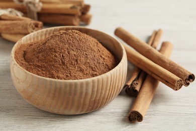 Aromatic cinnamon powder in bowl and sticks on white wooden table, closeup