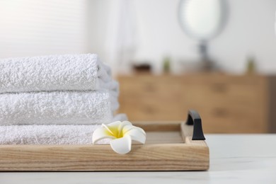 Photo of Wooden tray with stacked bath towels and beautiful flower on white table indoors. Space for text