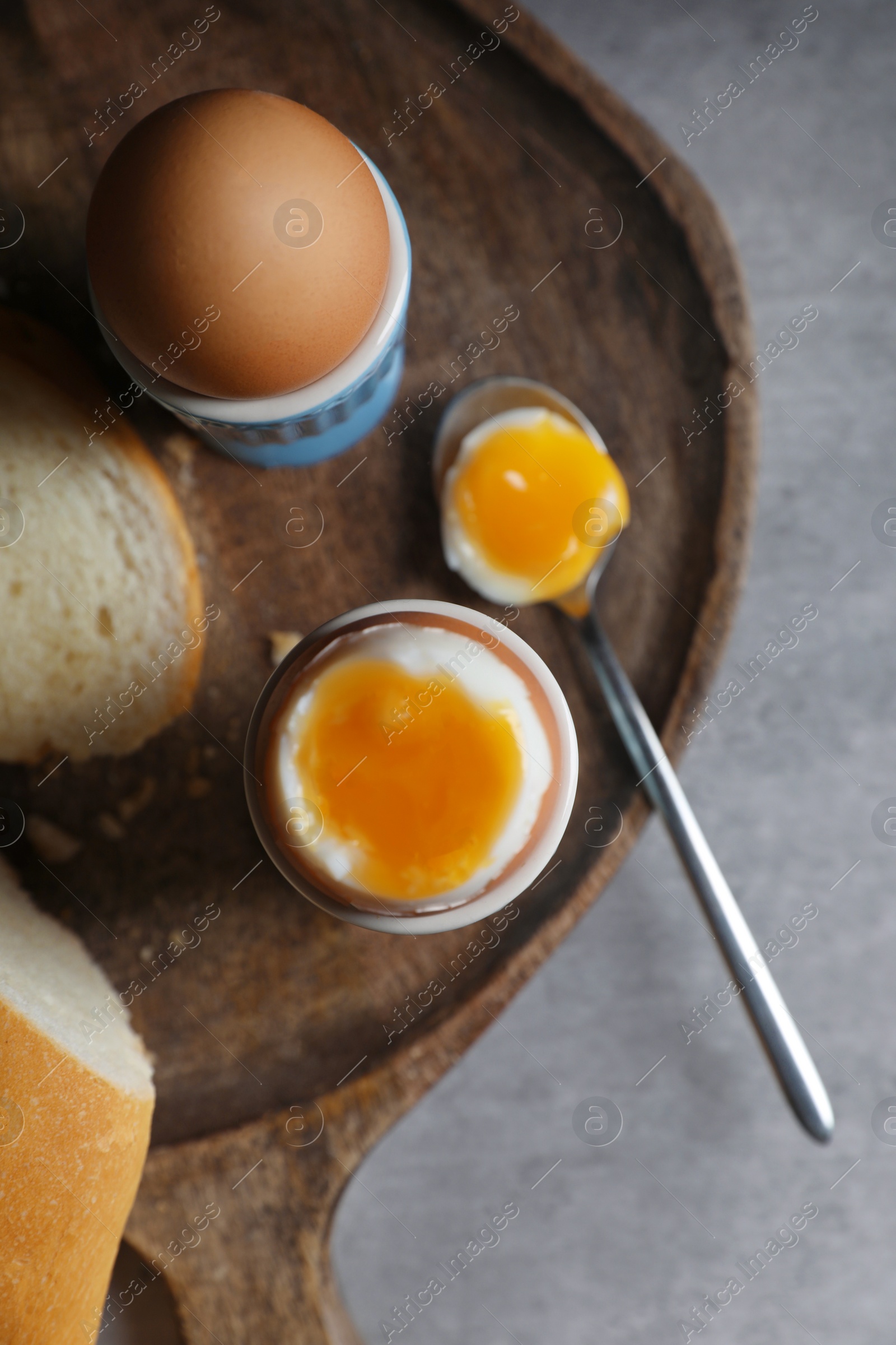 Photo of Fresh soft boiled eggs in cups and bread on grey table, flat lay