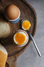 Fresh soft boiled eggs in cups and bread on grey table, flat lay