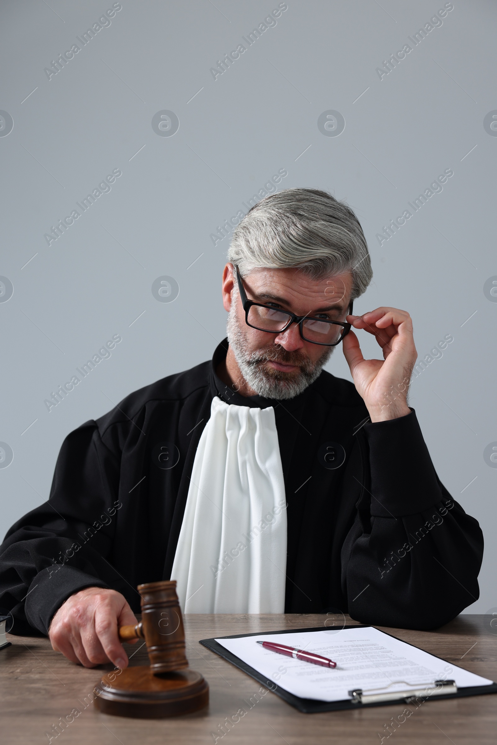 Photo of Judge with gavel and papers sitting at wooden table against light grey background