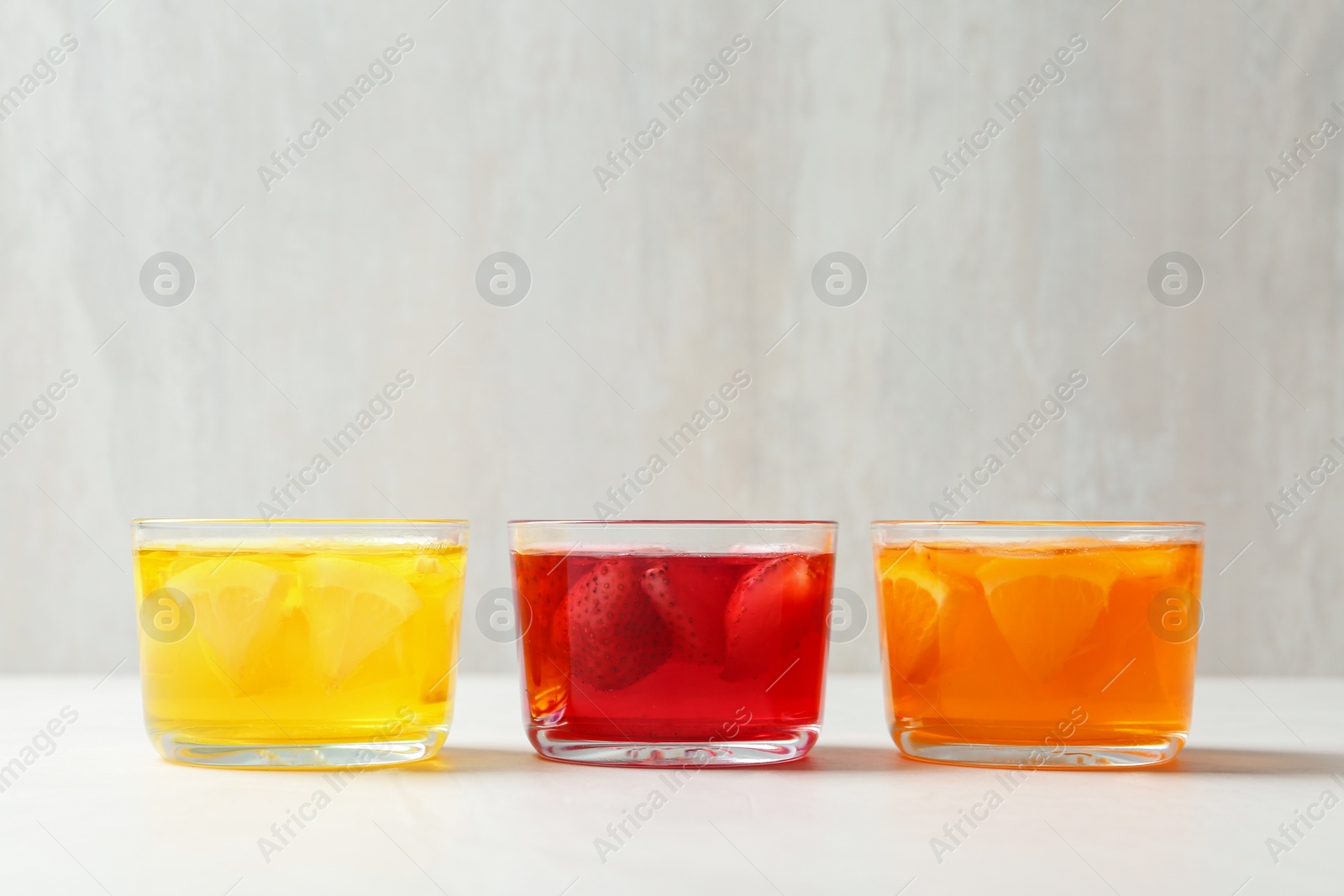 Photo of Glass bowls of natural jelly desserts on light table, space for text