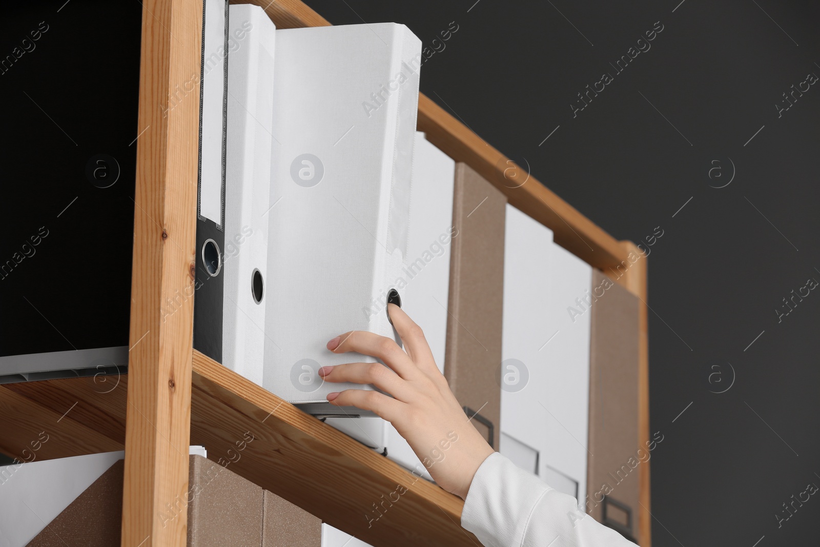 Photo of Woman taking folder with documents from shelf in office, closeup