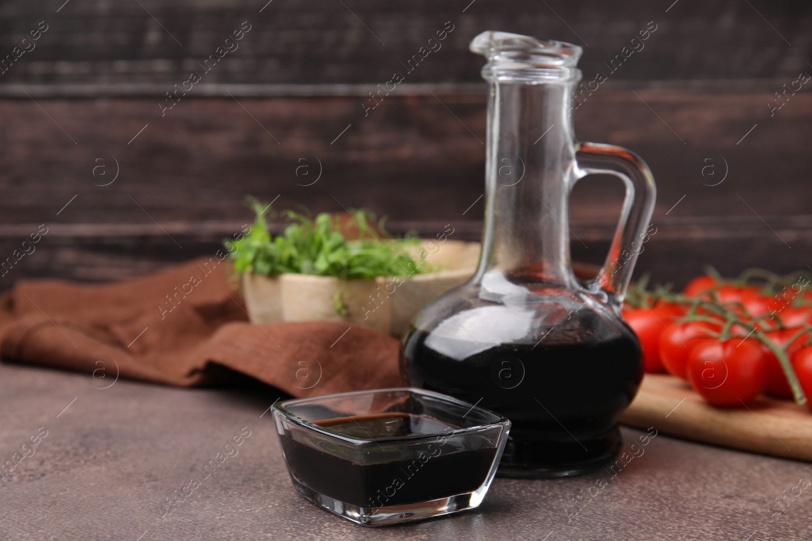 Photo of Organic balsamic vinegar, tomatoes and greens on grey table, space for text