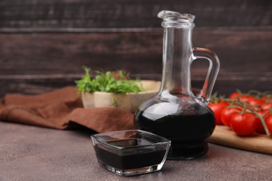 Photo of Organic balsamic vinegar, tomatoes and greens on grey table, space for text