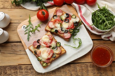 Photo of Tasty pizza toasts, sauce, arugula and tomatoes on wooden table, top view