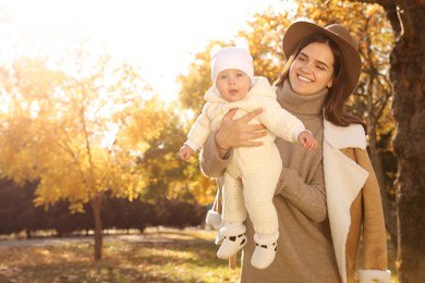 Happy mother with her baby daughter in park on sunny autumn day, space for text